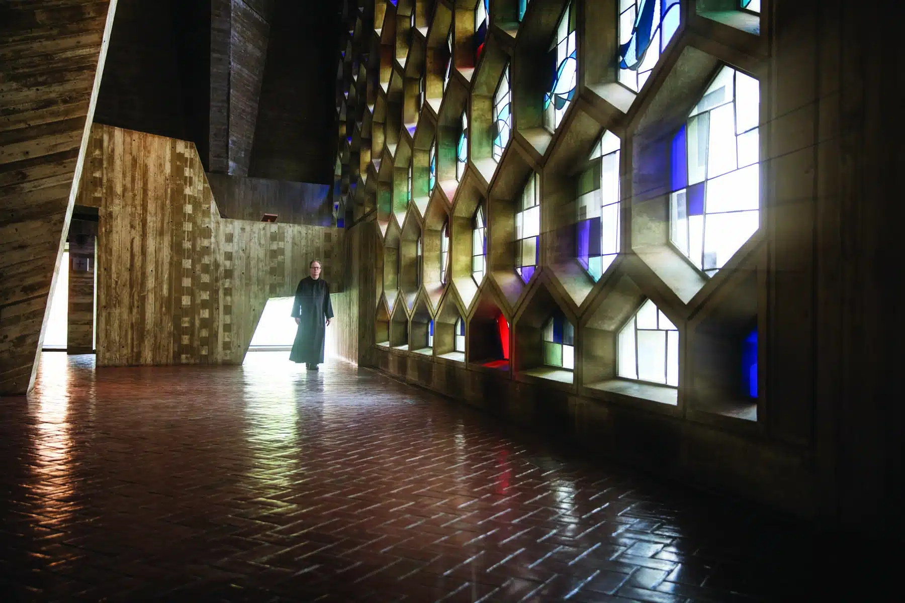 A monk walks past the honeycomb stained-glass wall of Marcel Breuer's abbey church at Saint John's Abbey